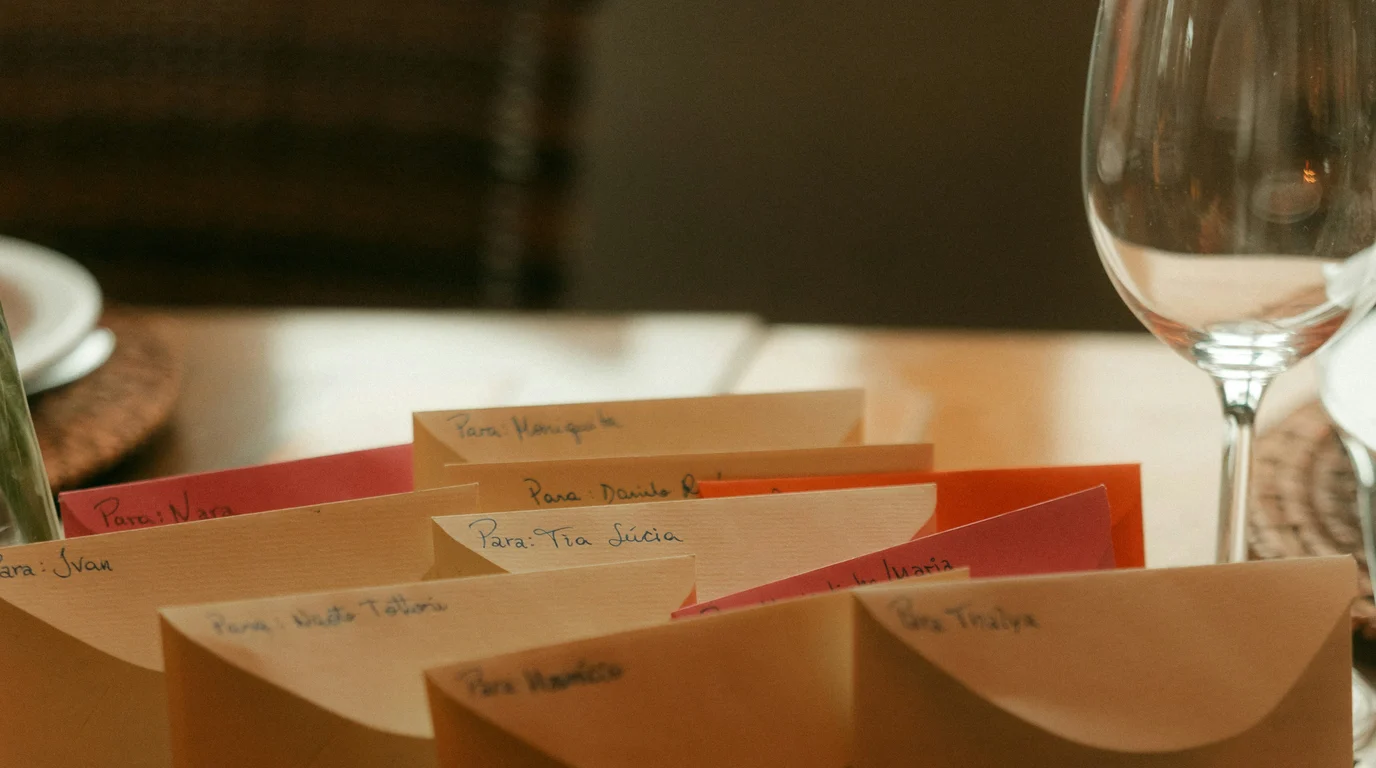 Handwritten place cards in cream, red and orange fanned across a warmly lit dining table beside empty wine glasses.