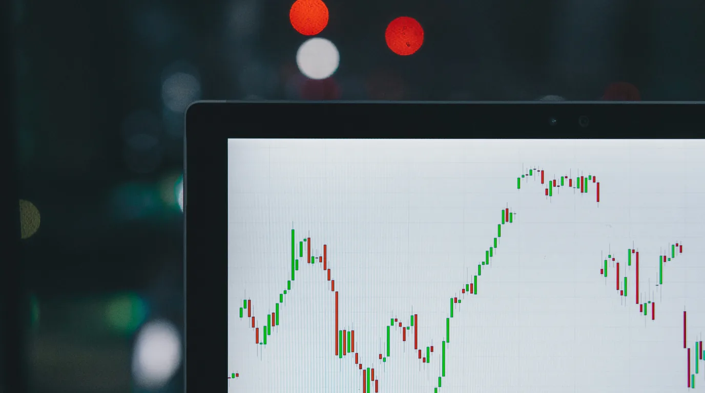 A laptop screen in a dim room showing a red and green candlestick chart.