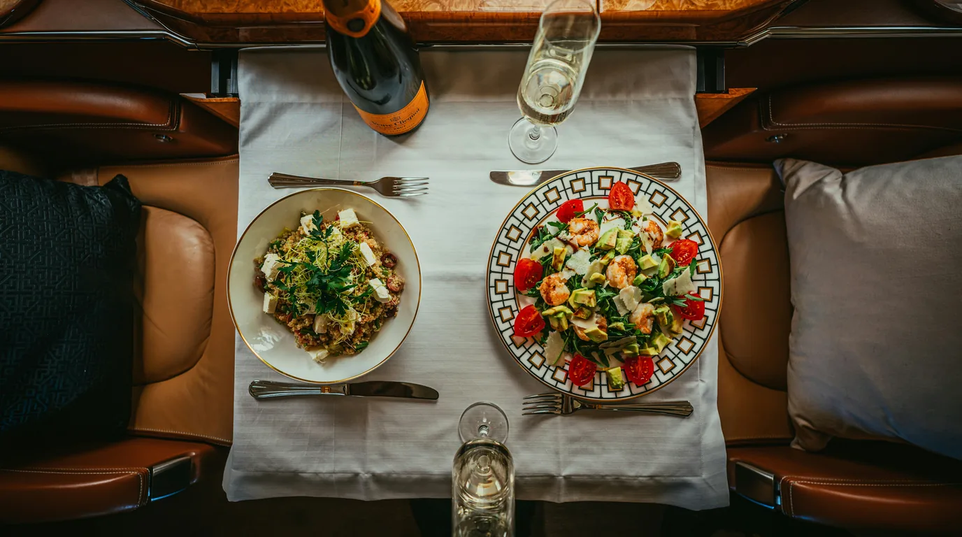 An airline tray table set with a salad, a green salad plate and two glasses on white linen.