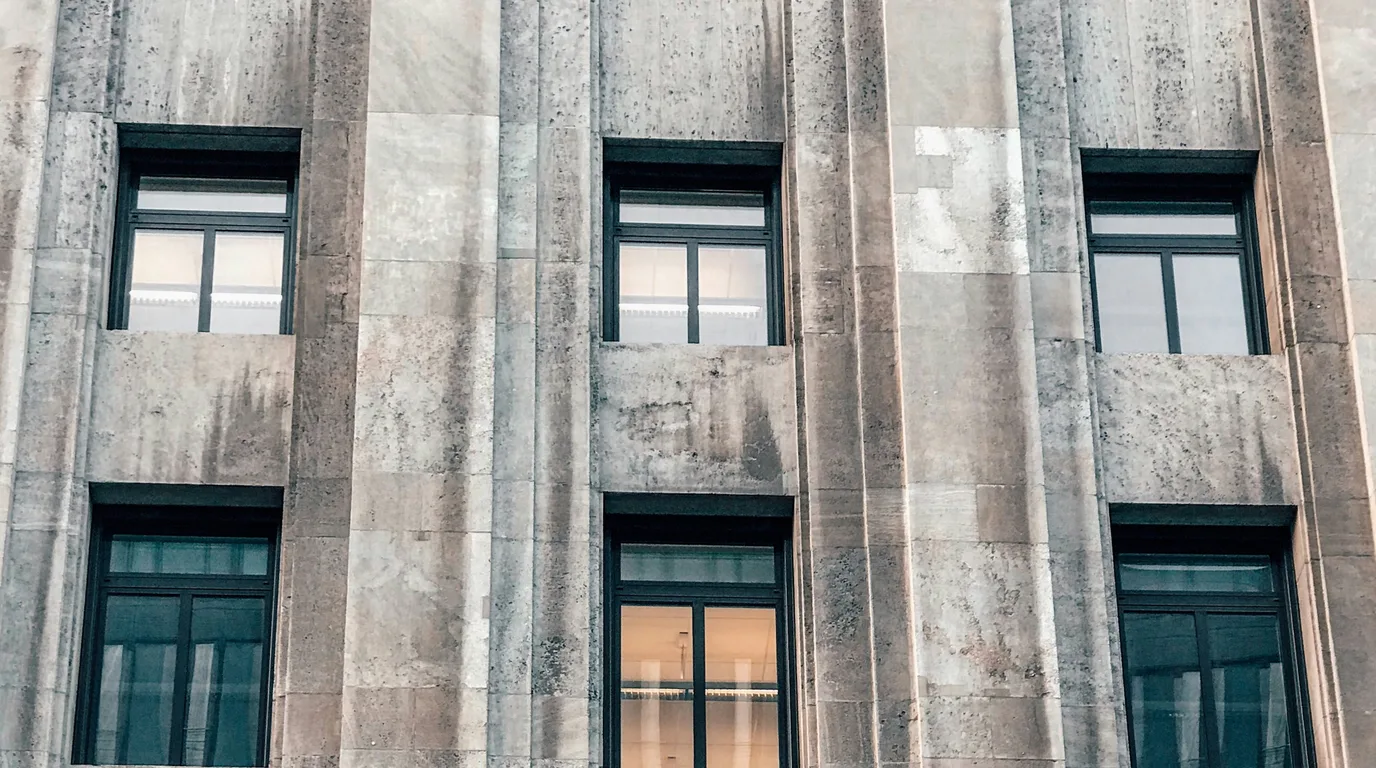 Tall dark windows set in a weathered stone facade, seen from below.