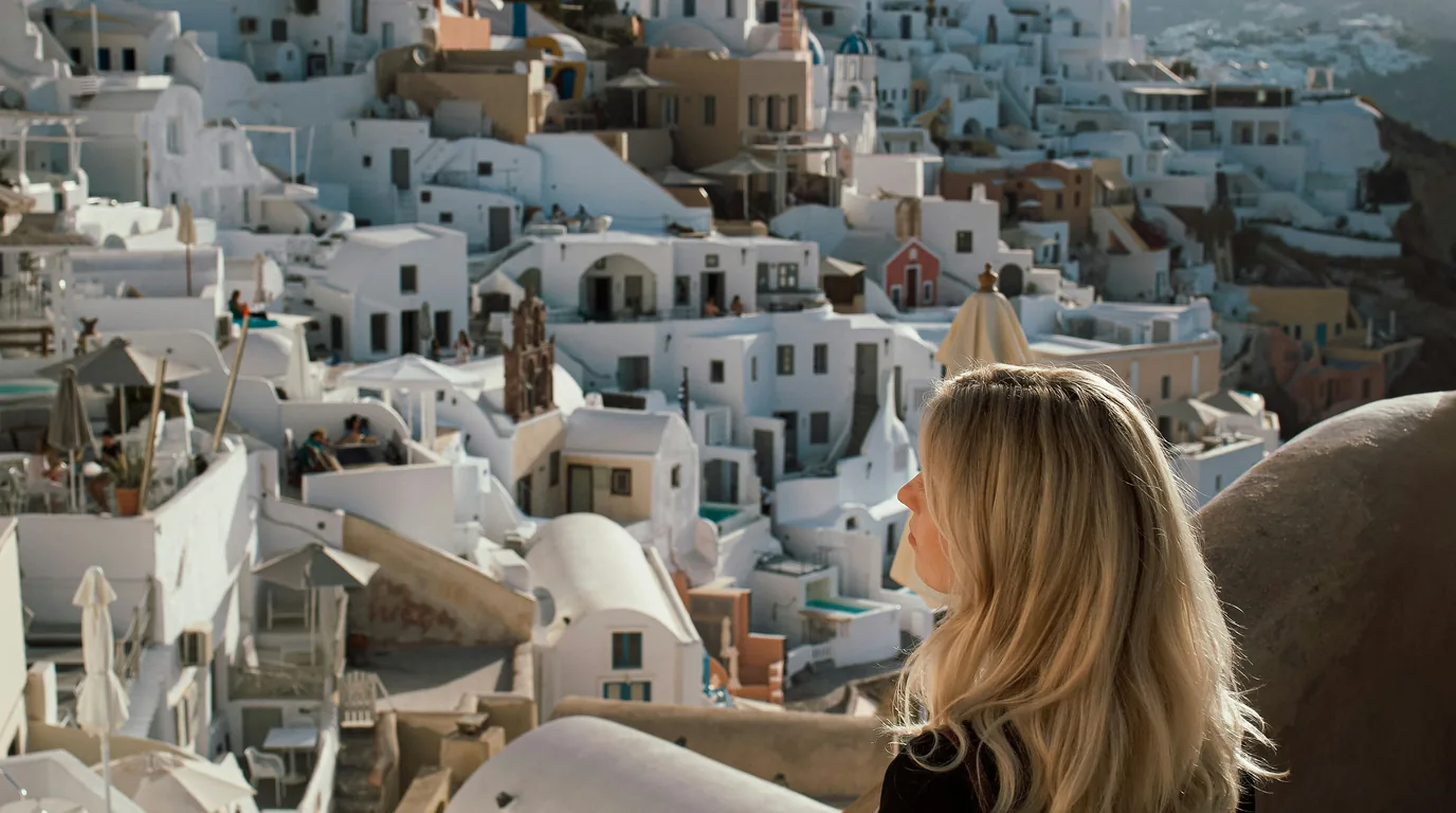 A woman looks out over the whitewashed cube houses and blue domes of a Greek island village.