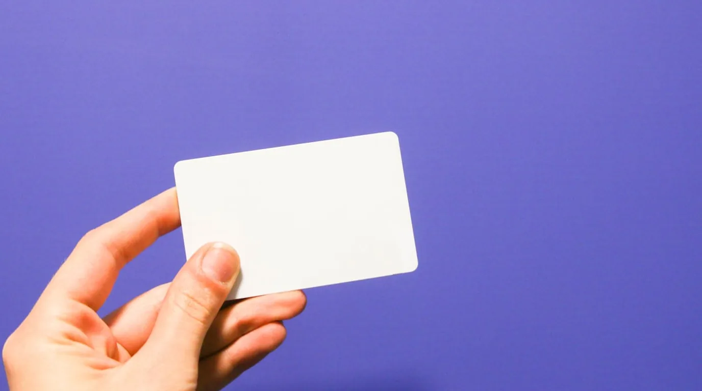 A hand holding a blank white card against a flat violet background.