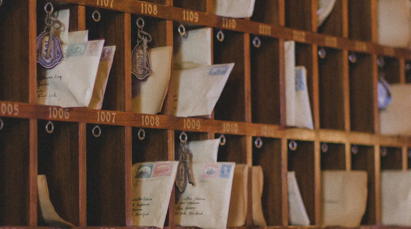A wooden pigeonhole rack of numbered compartments holding stamped envelopes and hanging key fobs.