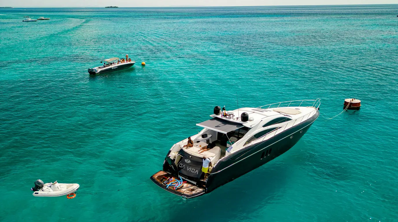 A white motor yacht and a small tender at anchor on flat turquoise water.