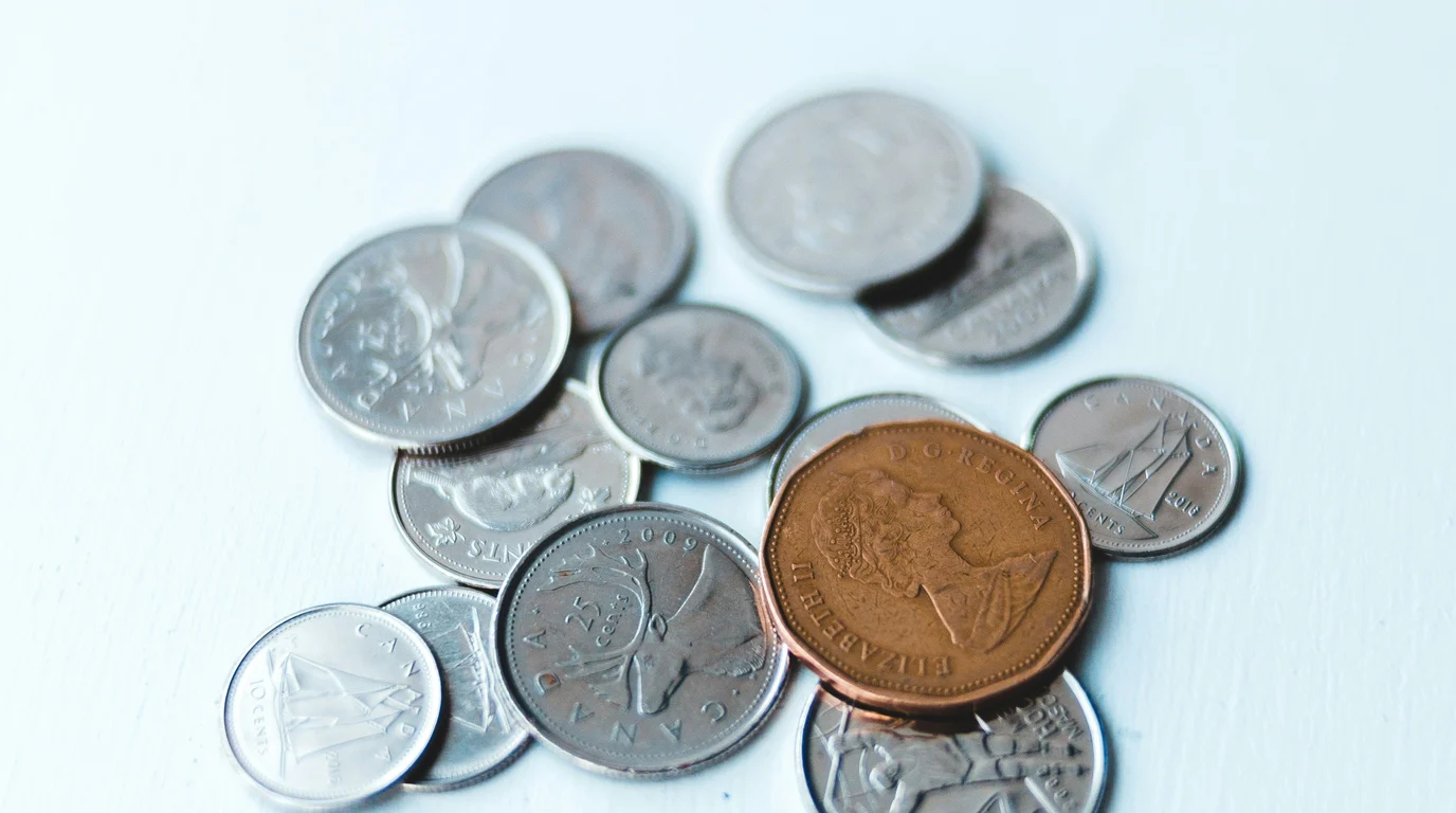 A small scatter of silver coins on a pale painted surface, with one larger copper coin catching the light among them.