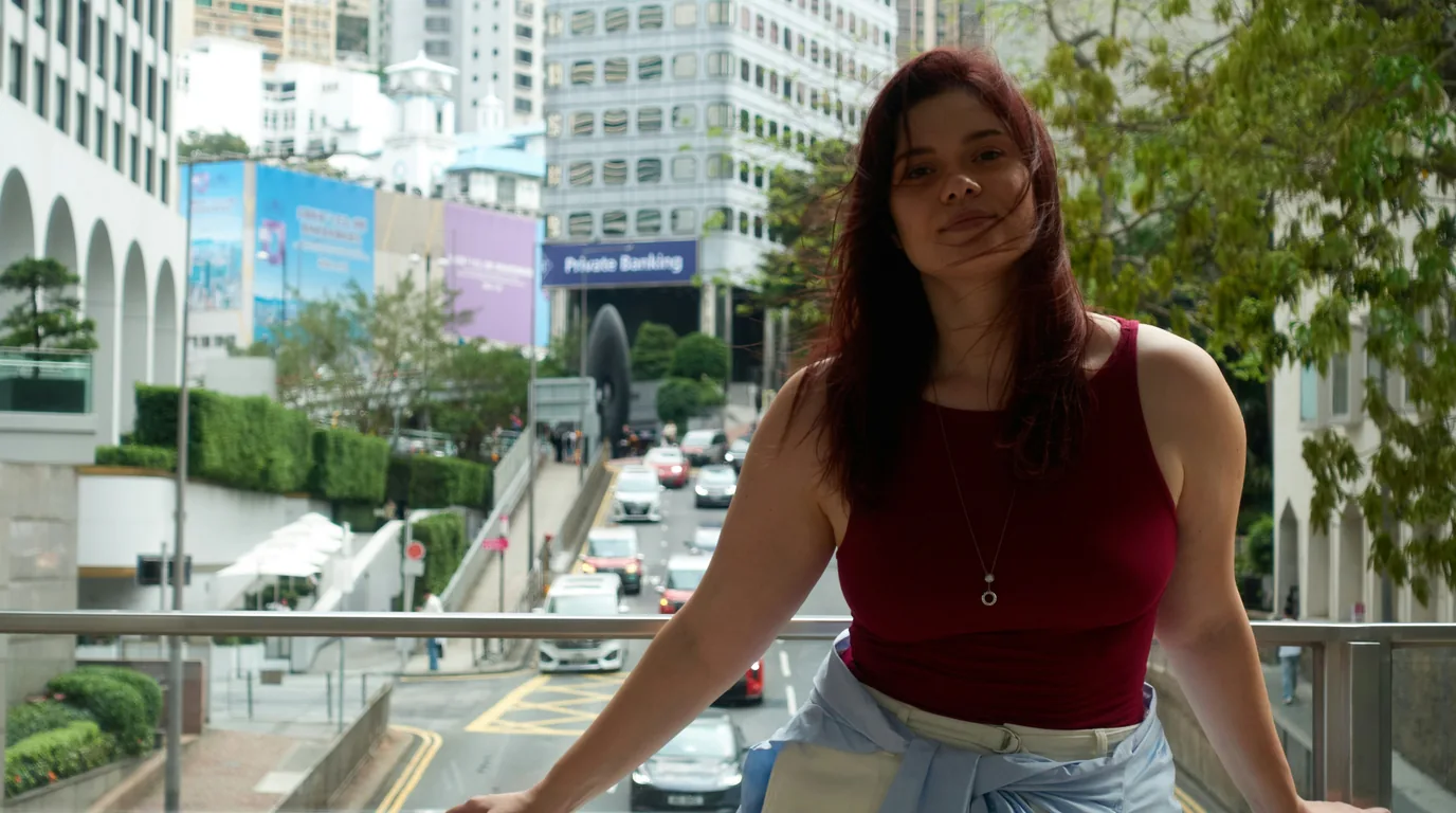 A woman on a raised walkway above city traffic, offices behind her.