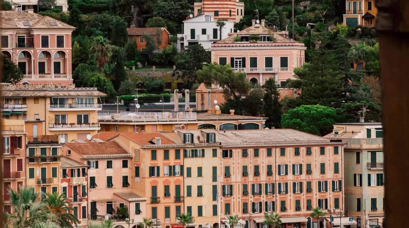 Pastel apricot and pink harbour buildings with green shutters rising above a Ligurian waterfront.
