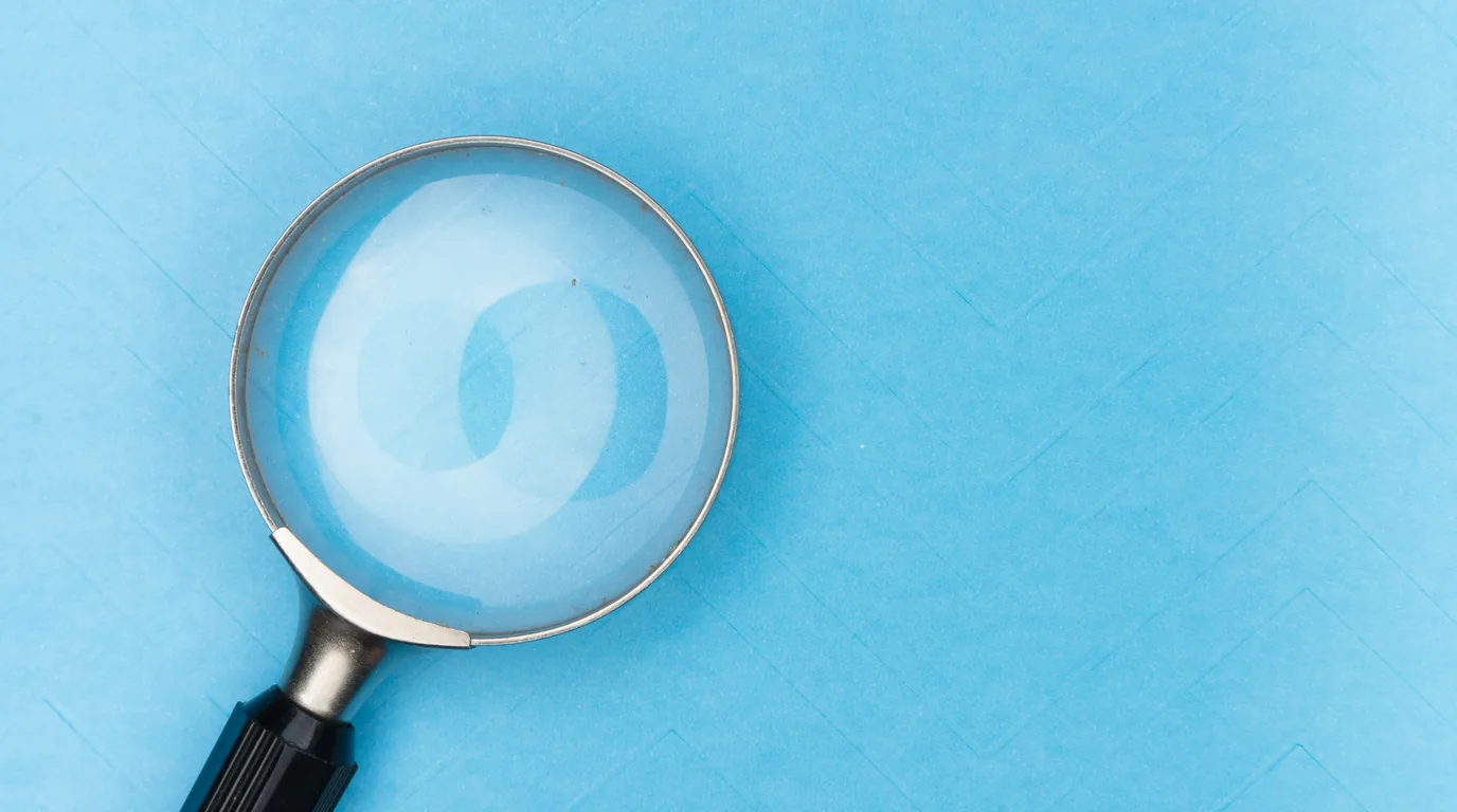 A magnifying glass lying on a flat pale blue surface.