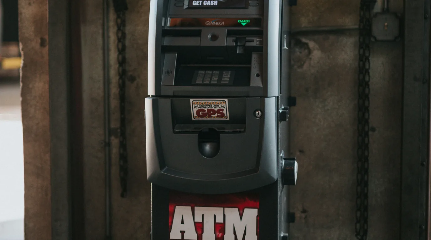 A cash machine under a security camera dome, a faded GET CASH panel above the slot.