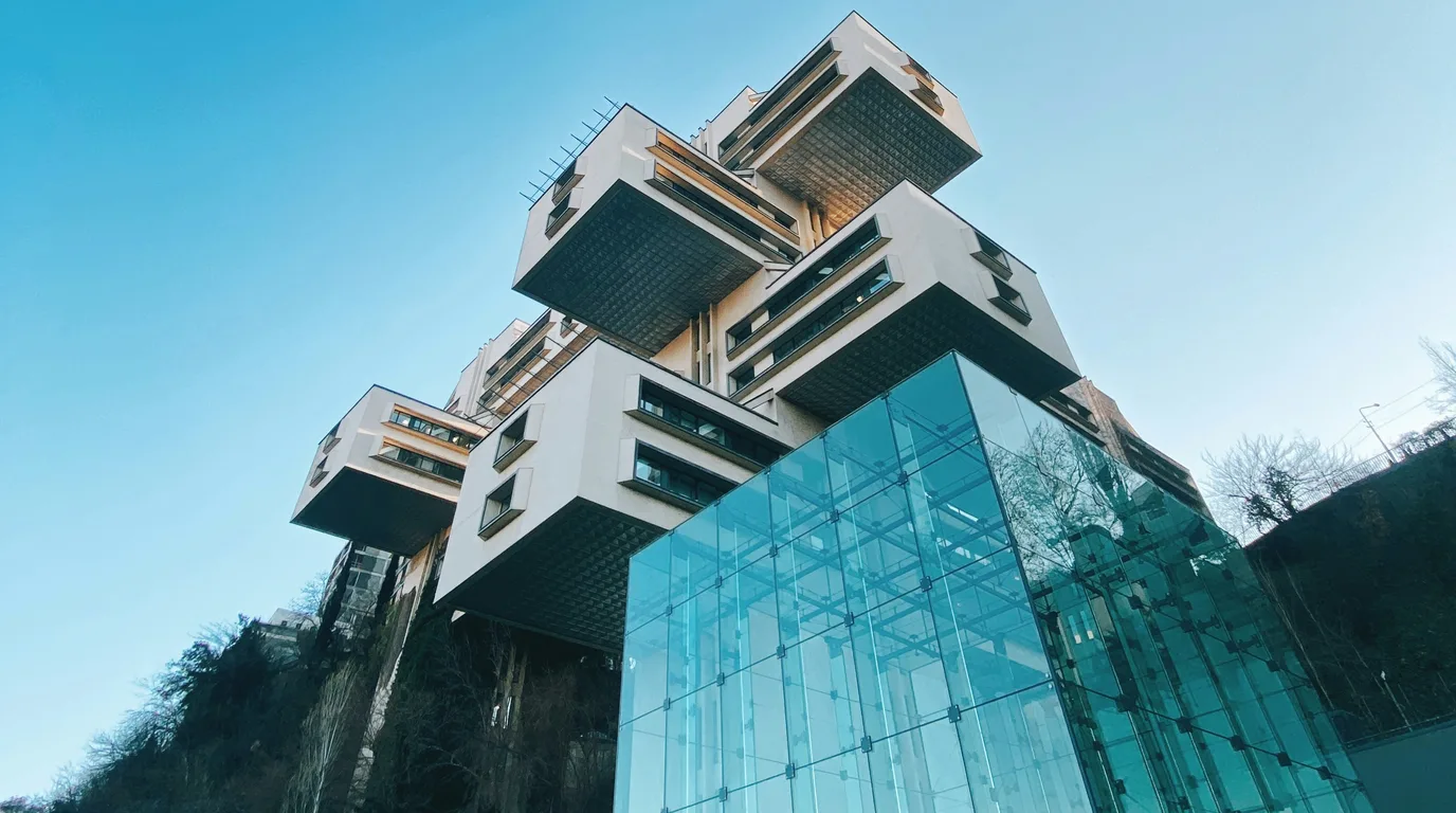 A cantilevered glass and concrete building seen from below against a clear sky.