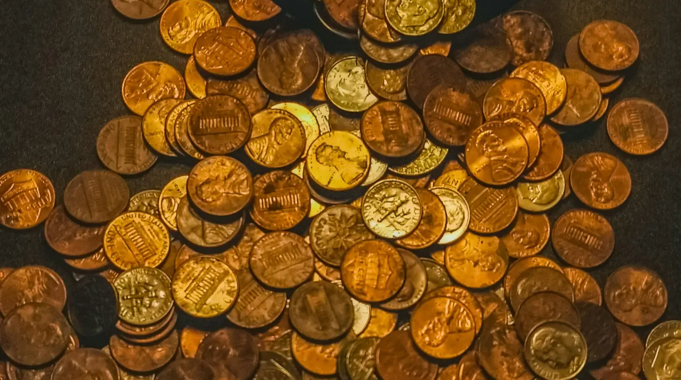 A dense scatter of copper and brass coins lying face up on dark cloth under warm golden light.