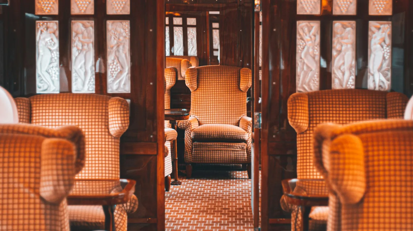 Orange wing-backed armchairs and panelled wood in the saloon of a vintage railway carriage.