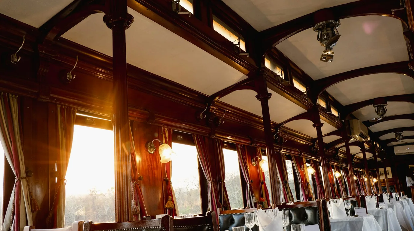 Set tables and brass wall lamps down the length of a mahogany dining car.