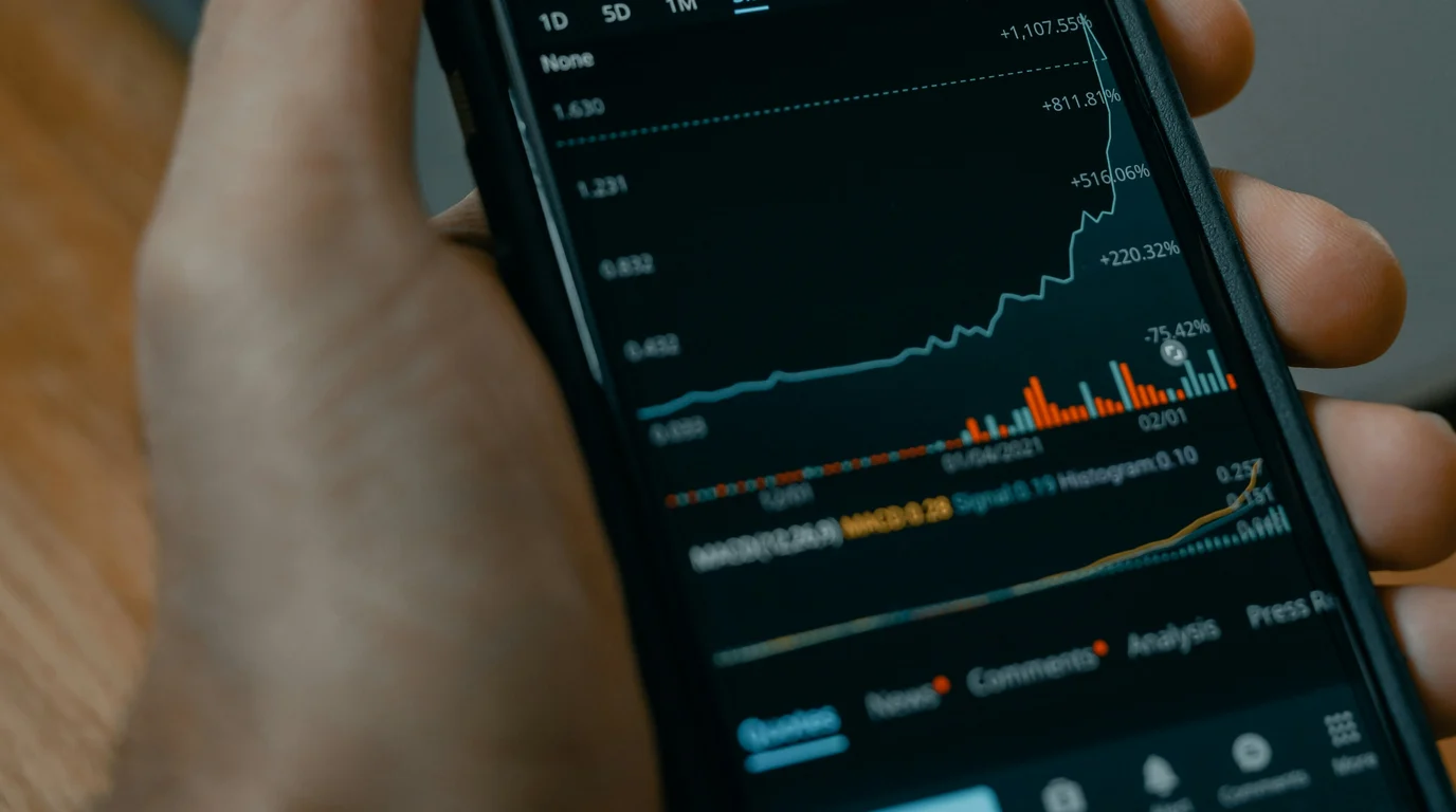 Fingers wrapped around a phone displaying a steeply rising dark-mode trading chart with coloured volume bars.