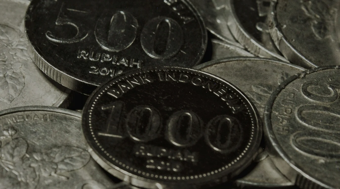 Worn silver coins stamped 1000 and 500 rupiah piled face up in a near-monochrome close-up.