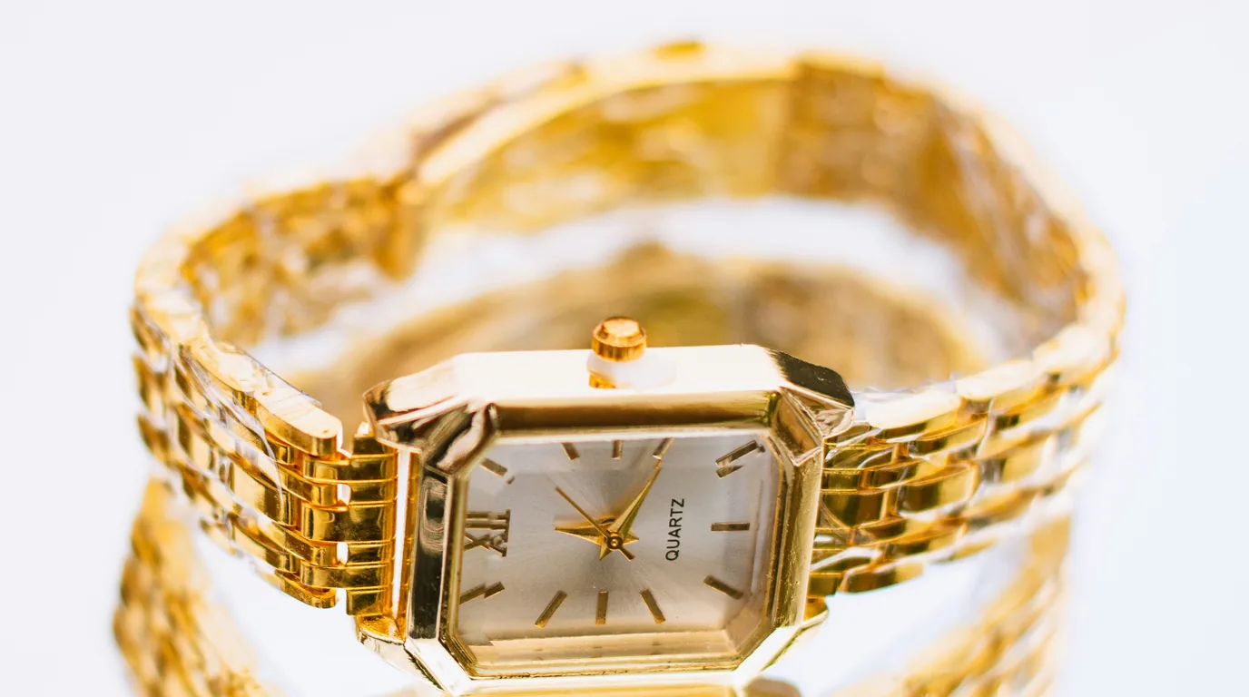 A gold-plated quartz wristwatch with a square case, laid flat on white.