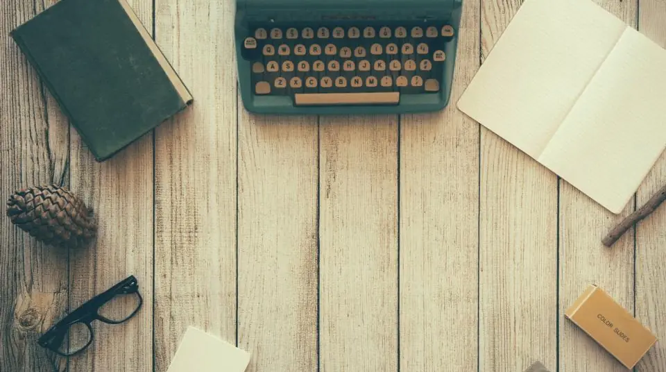 A vintage typewriter, notebooks and reading glasses on a wooden desk