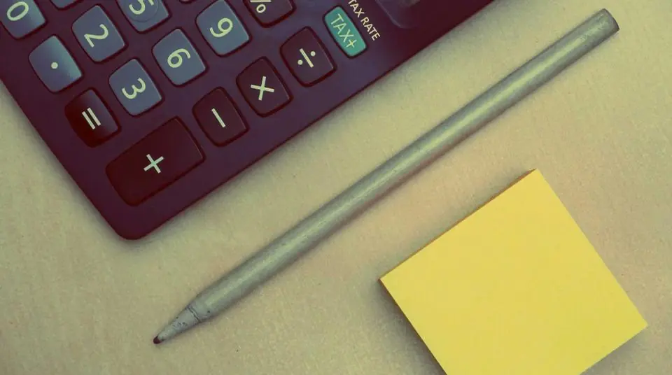 Close-up of a calculator keypad beside a pencil and a yellow sticky note